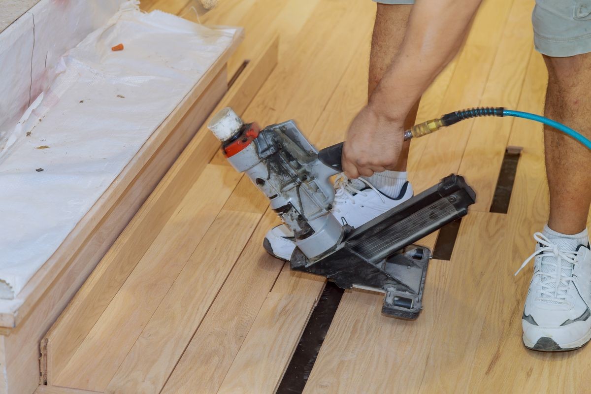 Handyman installing wooden floor in use pneumatic hammer new house